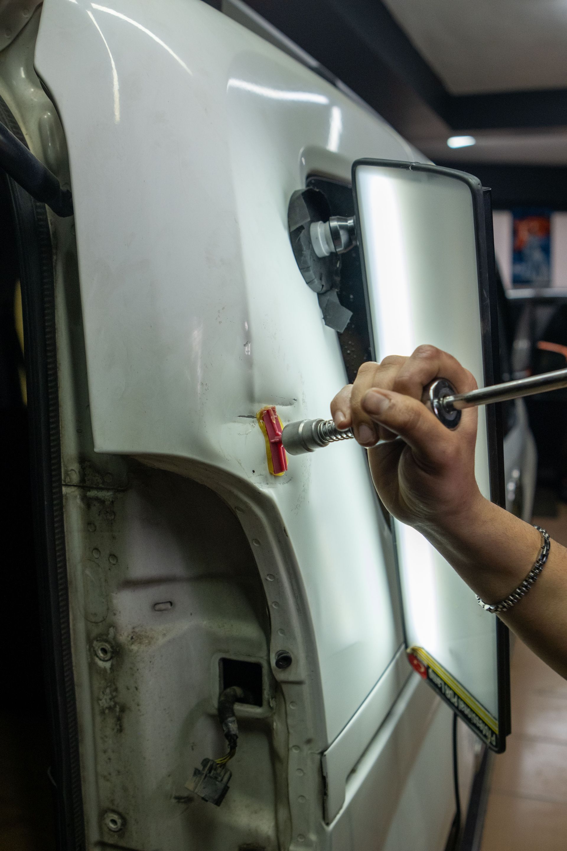 Close-up of vehicle dent repair in a garage using specialized tools under bright lighting.